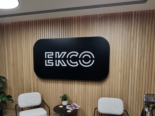 An illuminated black and white reception sign which reads ECKO with two chairs below it