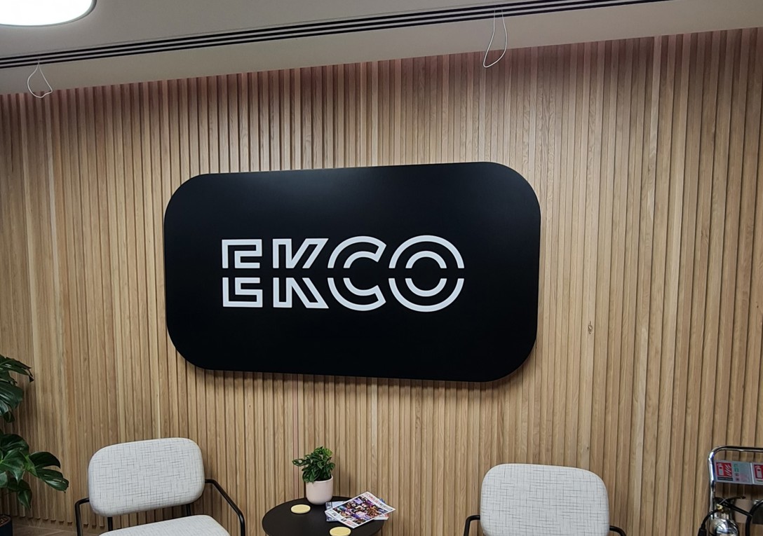 An illuminated black and white reception sign which reads ECKO with two chairs below it