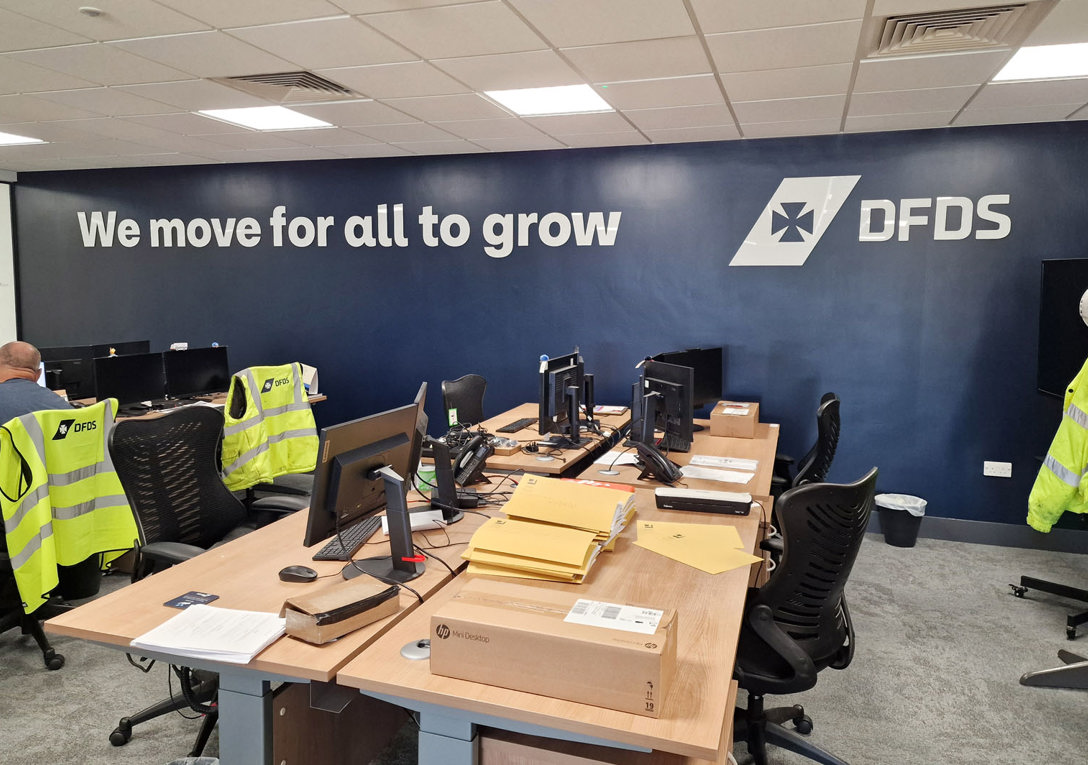 Office wall sign with gloss white acrylic lettering and logo applied onto the dark blue wall at the new DFDS Peterborough premises.  